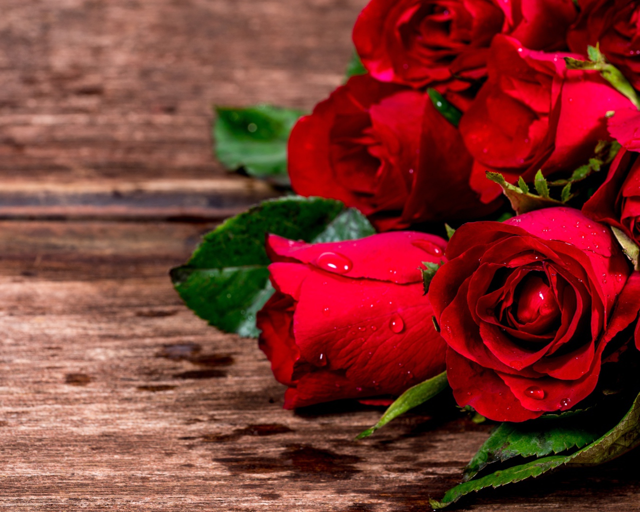 Букет красных роз на деревянном столе в каплях воды