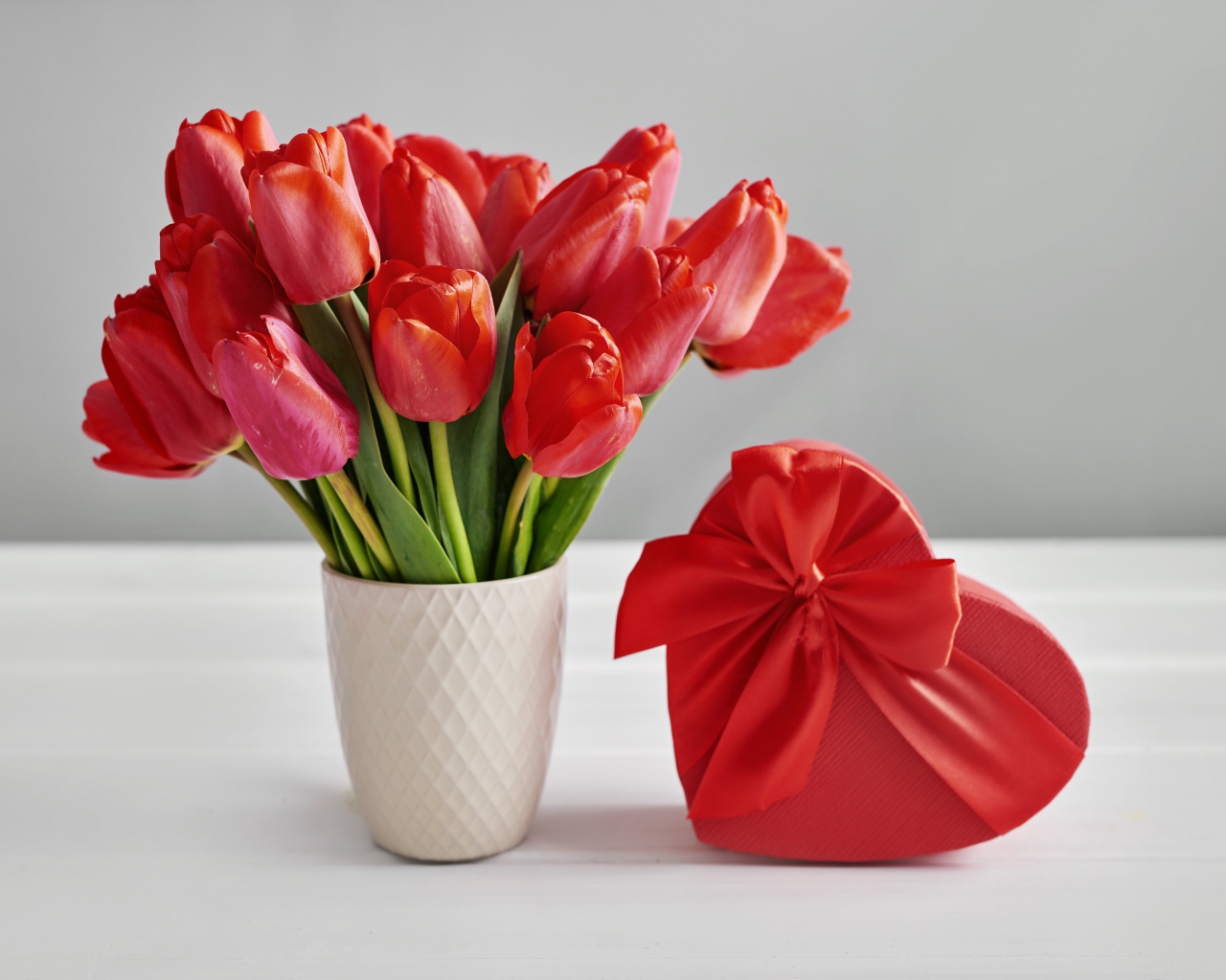 Bouquet of red tulips on a table with a heart-shaped box