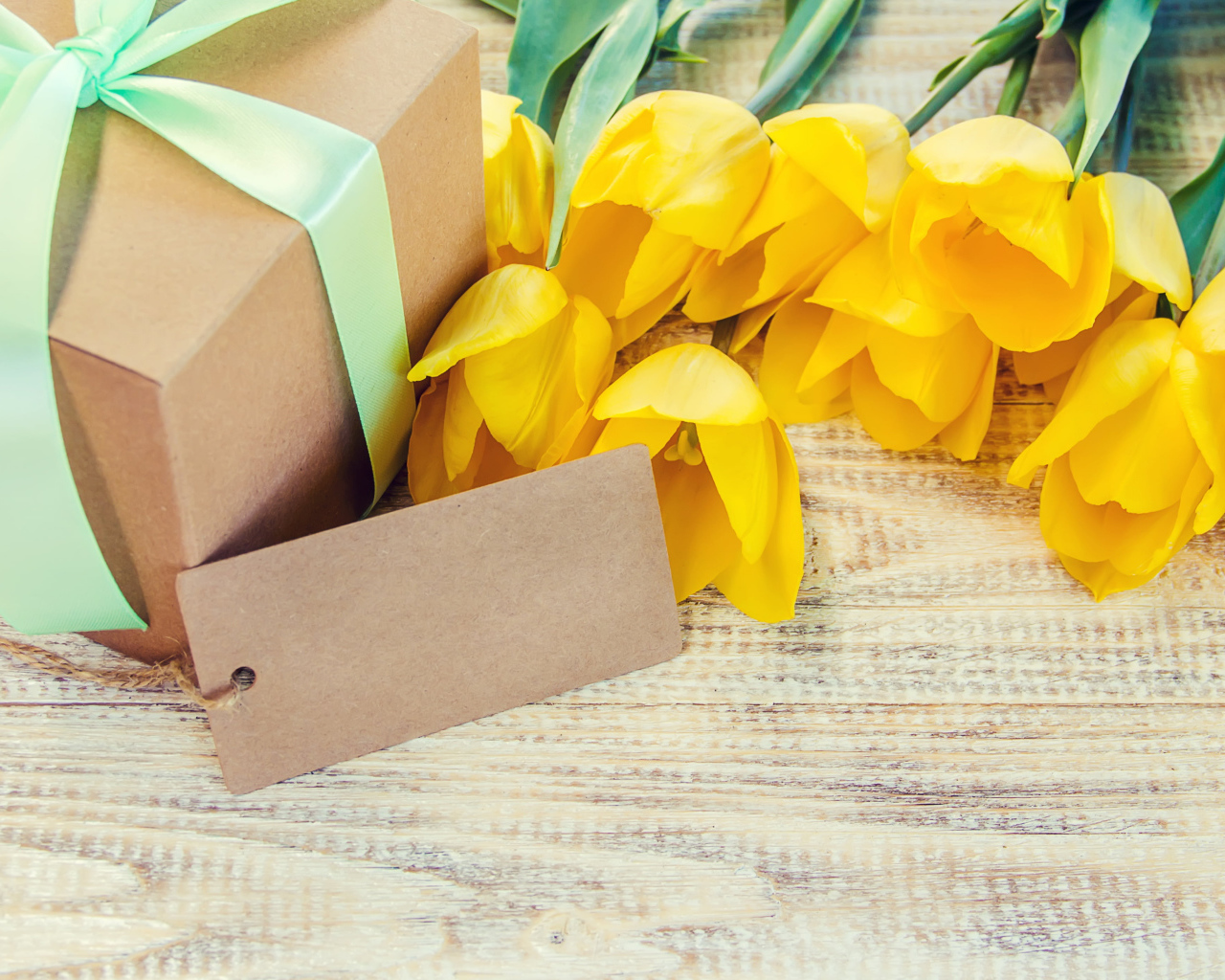 Букет желтых тюльпанов с подарком на столе 