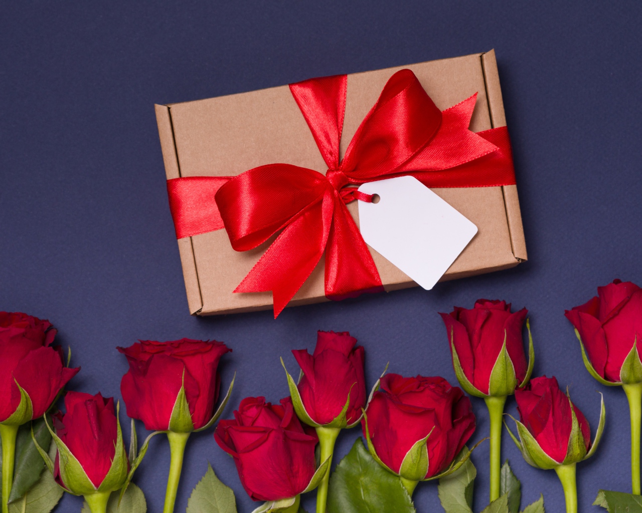 Подарок с красным бантом на столе с розами