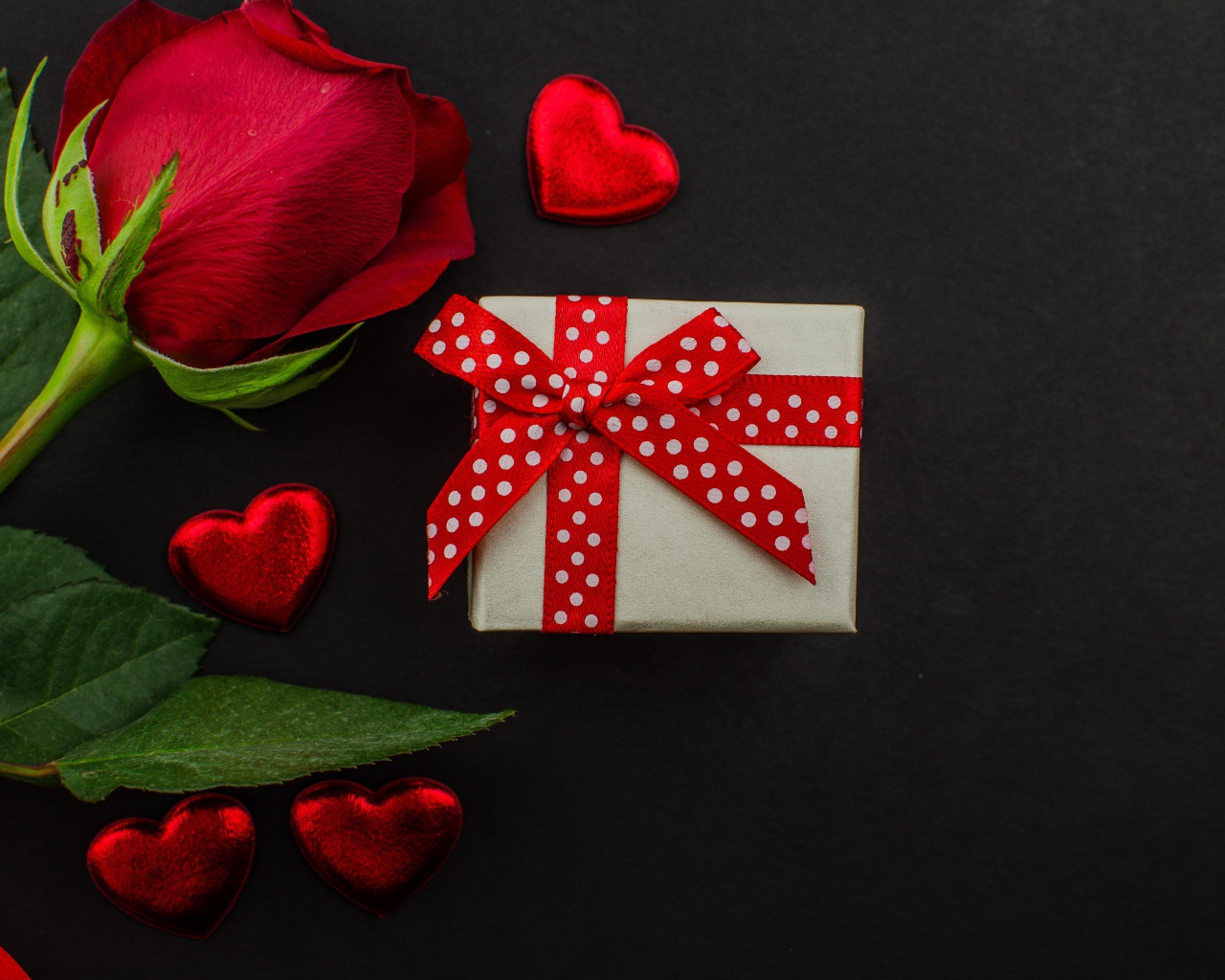 Маленький подарок и красная роза на черном столе