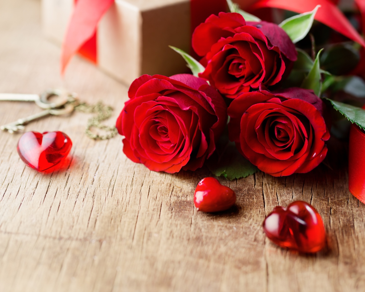 Три красивые красные розы на столе с сердечками и ключами