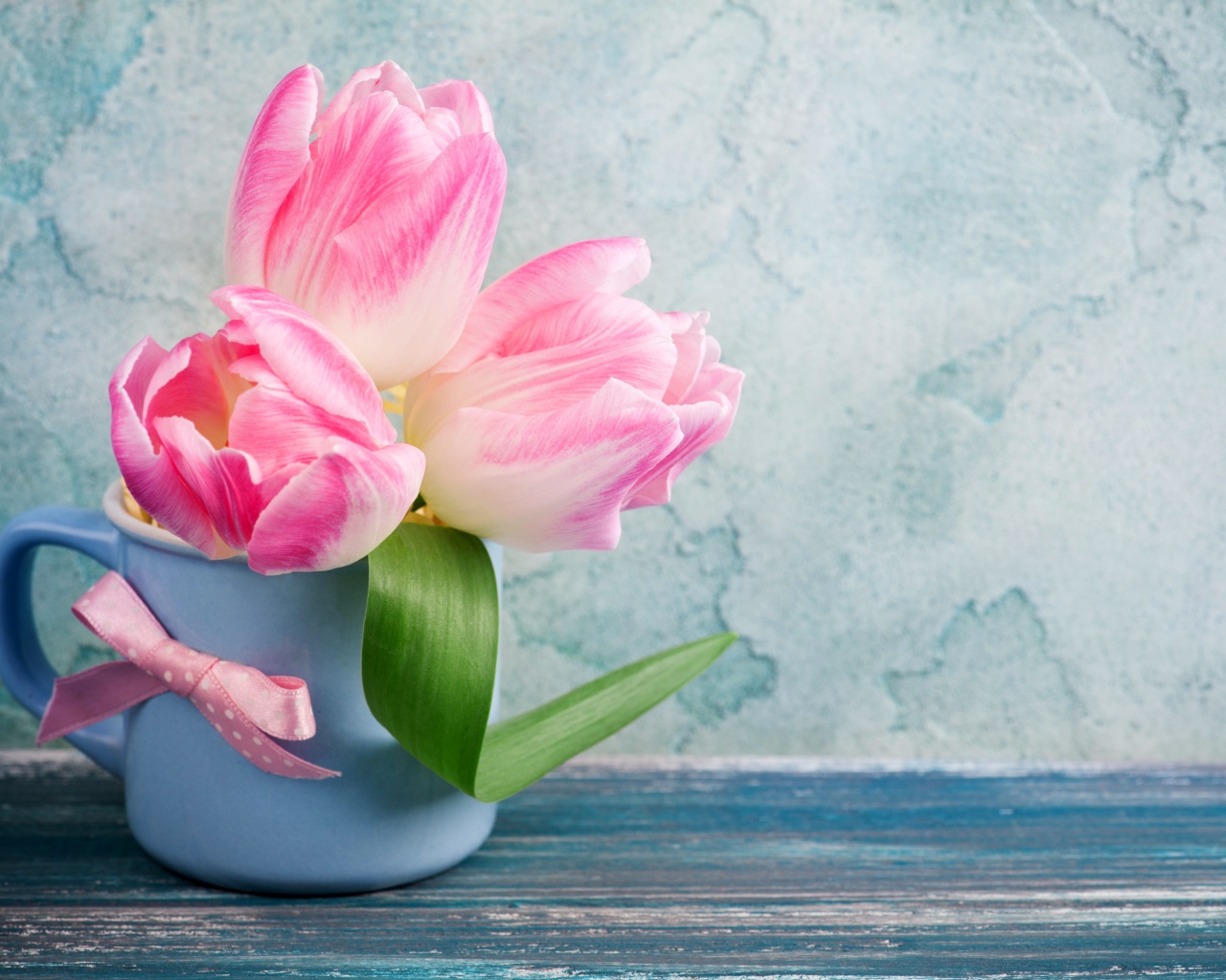 Три розовых тюльпана в чашке на столе 
