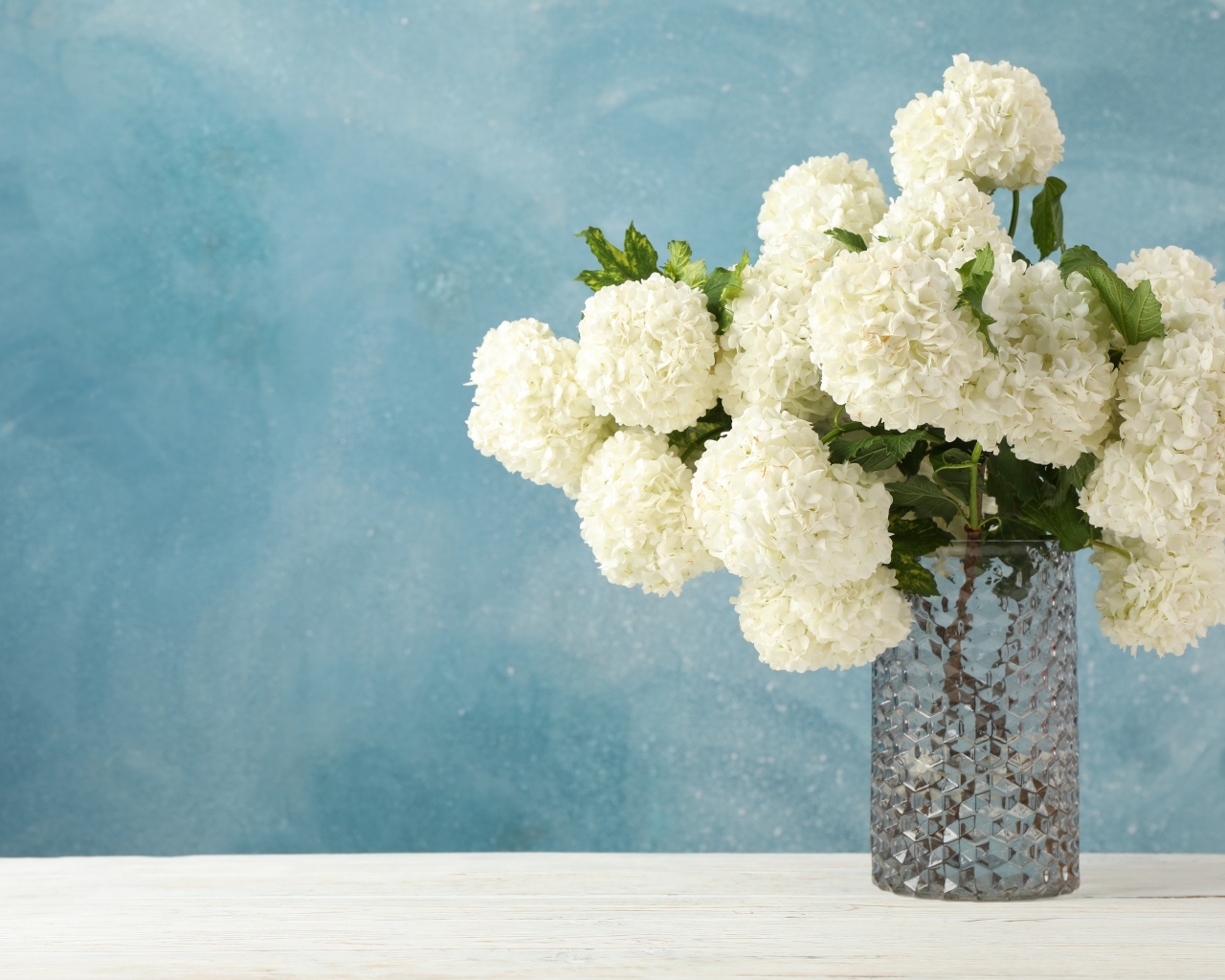 Белые цветы гортензии в стеклянной вазе на столе 