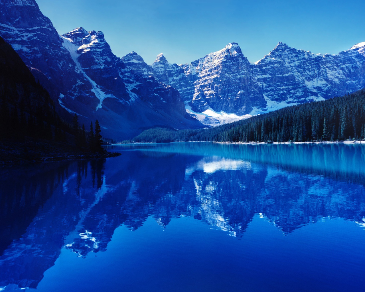 Высокие заснеженные горы отражаются в воде озера 