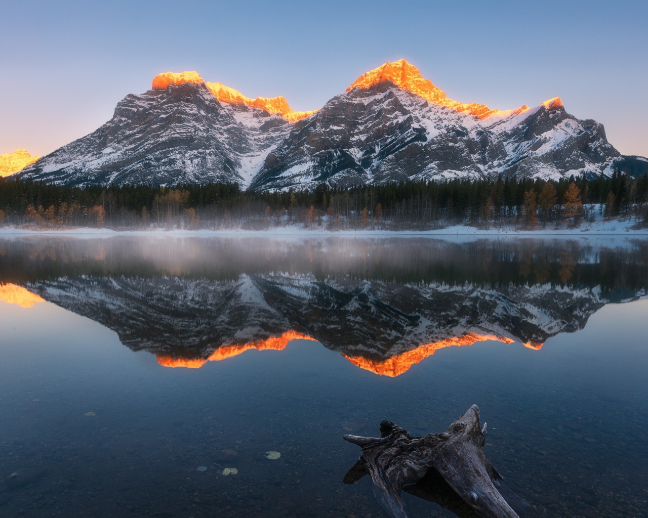 Вершины гор в лучах солнца отражаются в чистой воде озера