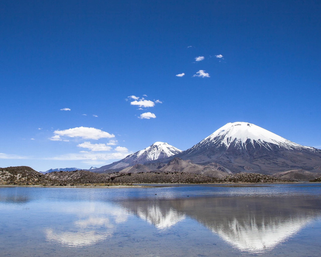 Заснеженные вершины гор под голубым небом отражаются в воде 