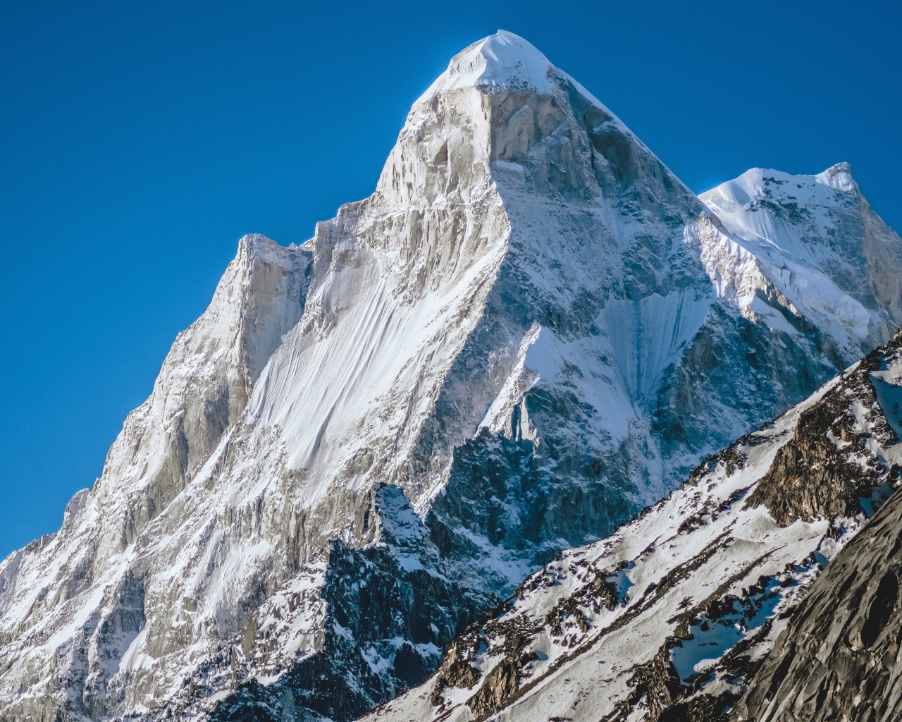 Острая вершина заснеженной горы под голубым небом