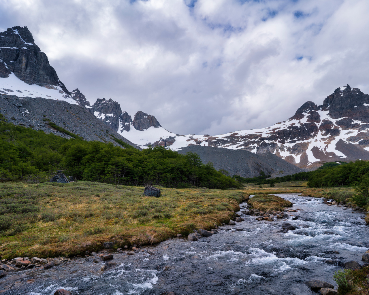 Быстрая река у заснеженных гор под густыми белыми облаками