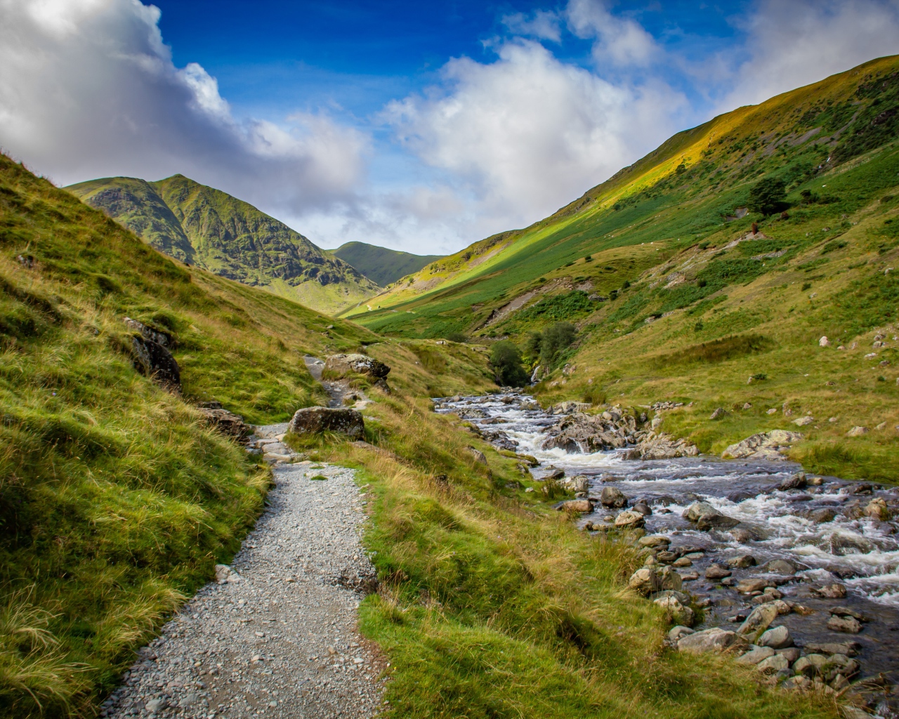 Тропа у реки на фоне покрытых зеленью гор 