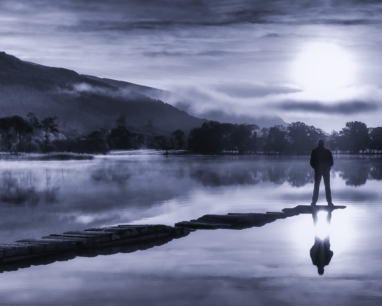 Мужчина стоит на мосту у озера ночью при свете луны