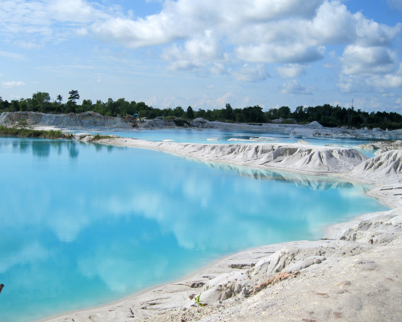 Белый песок на берегу водоема с голубой водой 