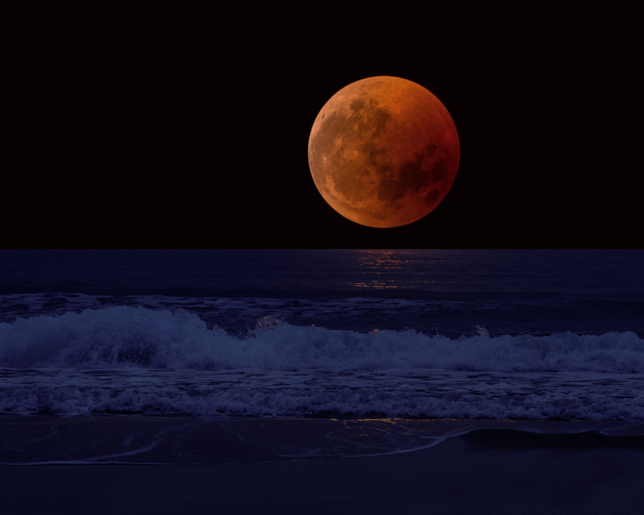 Big red moon in the dark sky over the sea