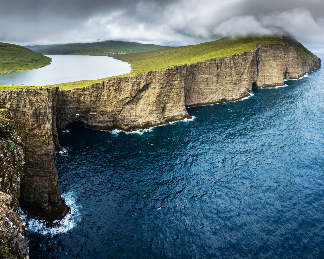 Океан омывает зеленый утес под пасмурным небом