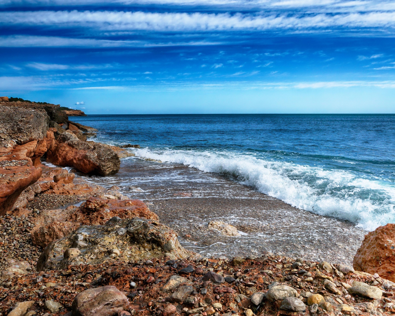 White waves by the sea with large stones under a blue sky