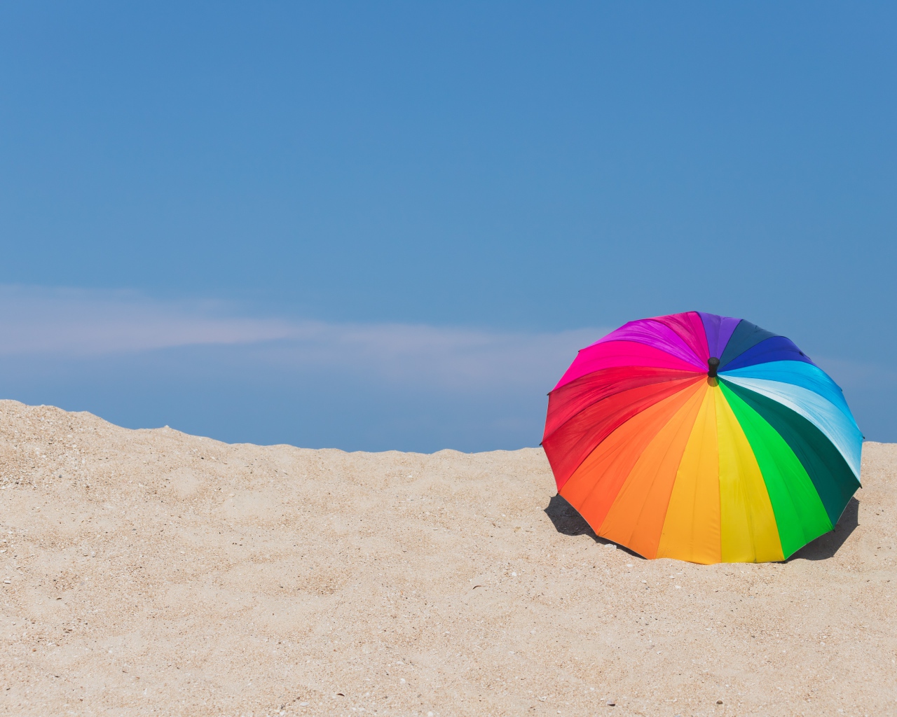 Разноцветный зонт лежит на горячем песке летом