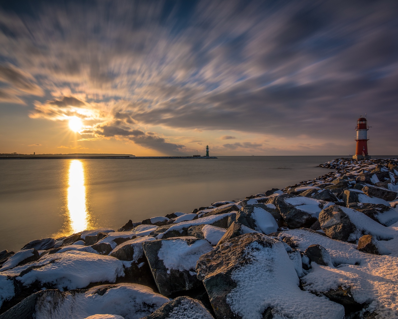 Заснеженные камни на берегу моря с маяком на закате