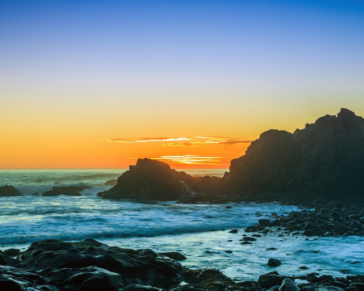 Закат солнца над океаном с камнями на берегу 