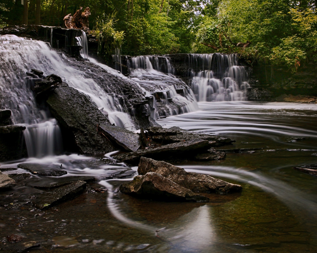 Быстрая вода стекает по камням водопада в парке 