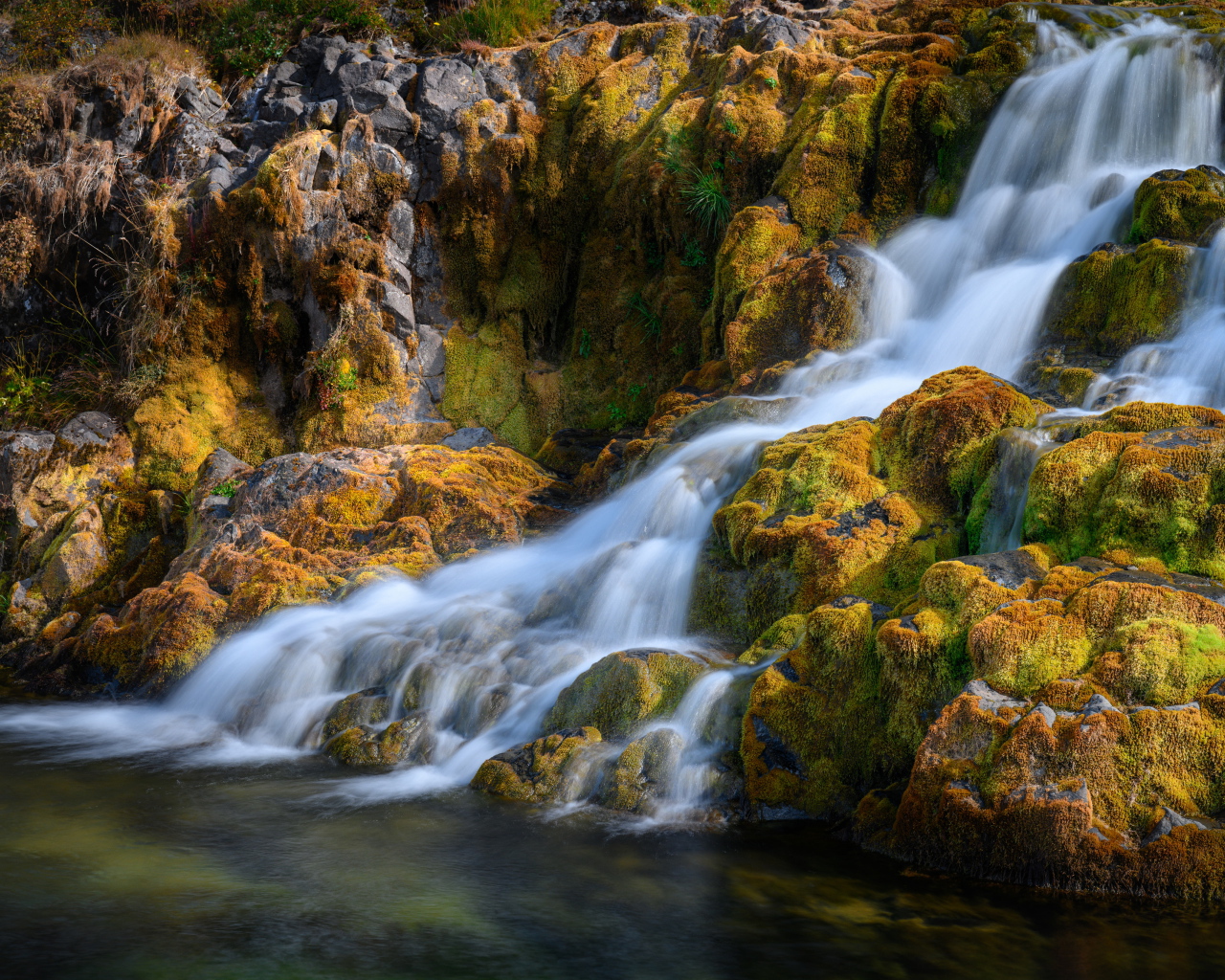 Быстрая вода водопада стекает по покрытым мхом камням, Исландия 