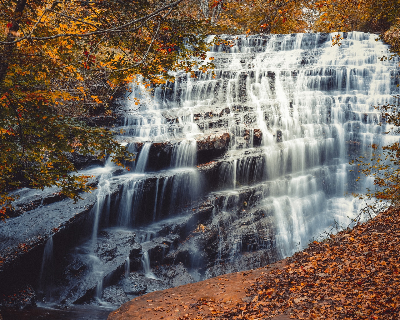 Быстрая вода водопада стекает по каскадам камней осенью