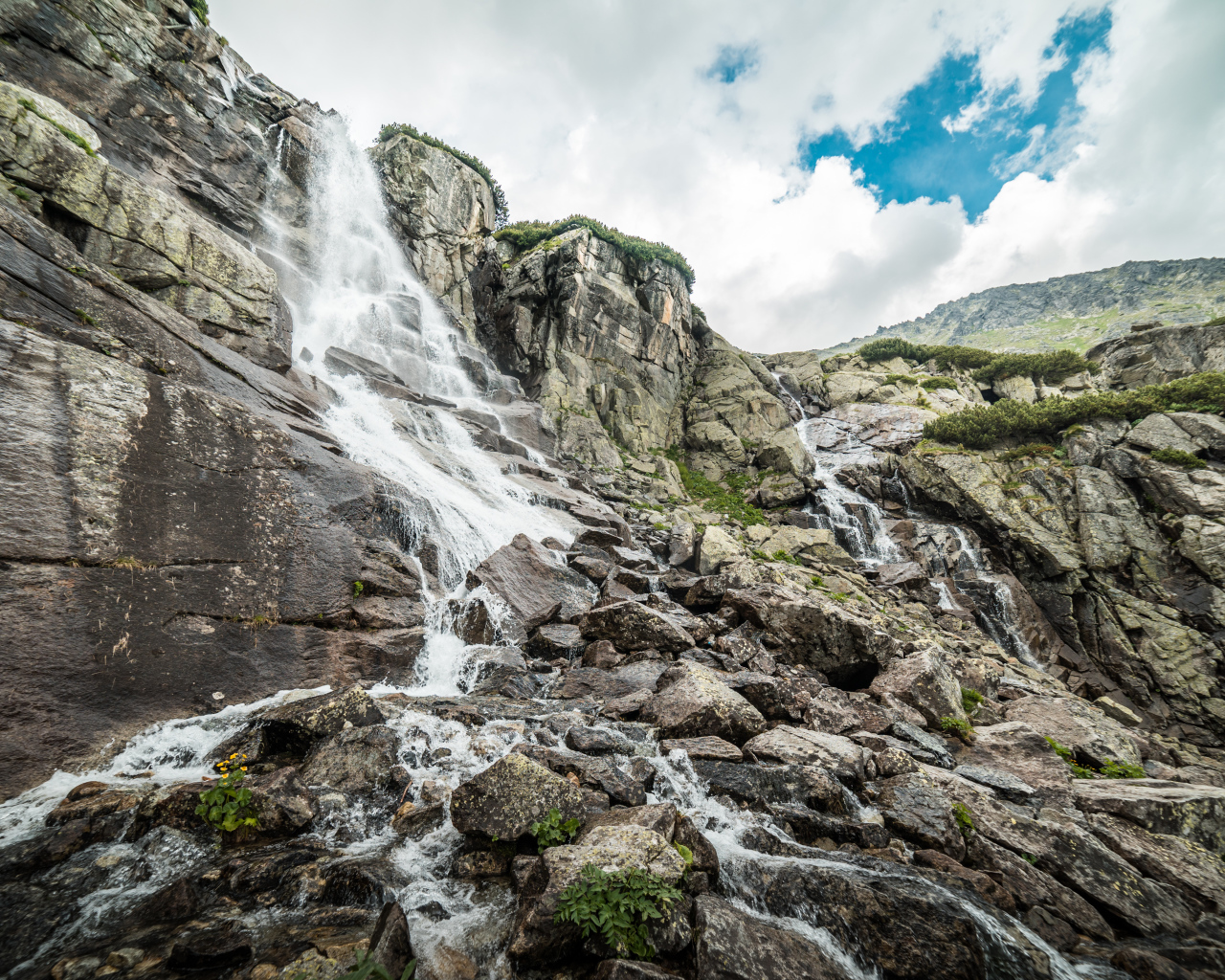 Водопад стекает по камням на фоне неба с белыми облаками