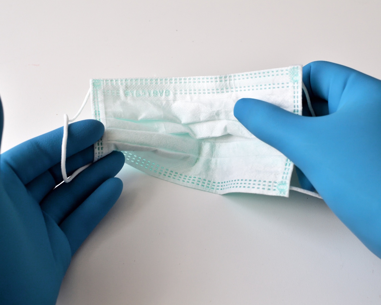 Руки в медицинских перчатках держат маску 