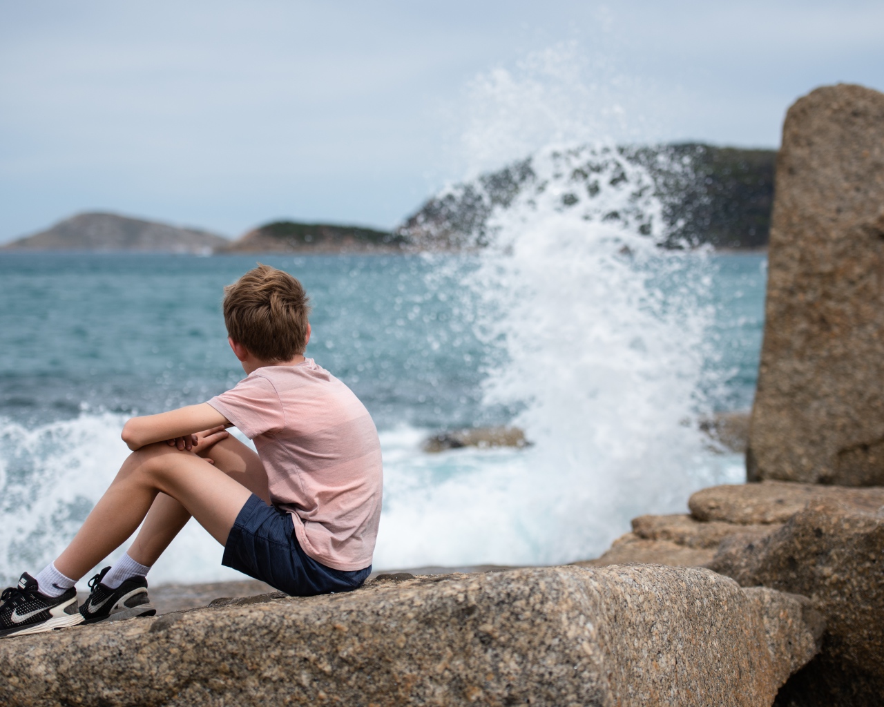 Мальчик сидит на камнях у бушующего моря