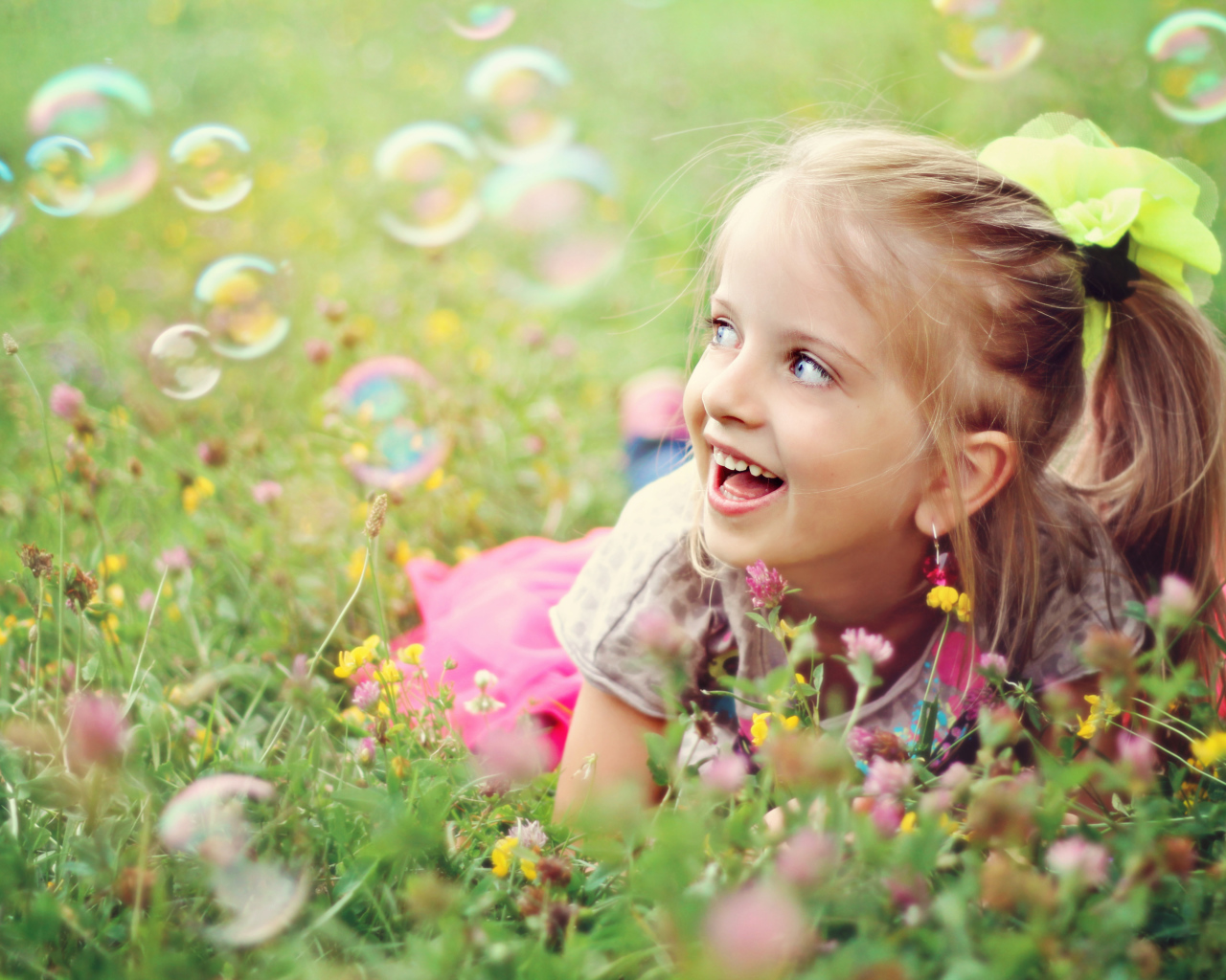 Веселая девочка лежит на траве с мыльными пузырями