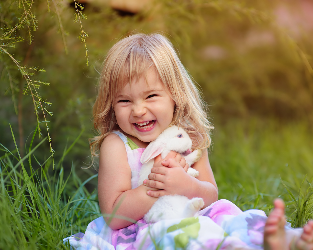 Довольная маленькая девочка обнимает белого кролика на траве 