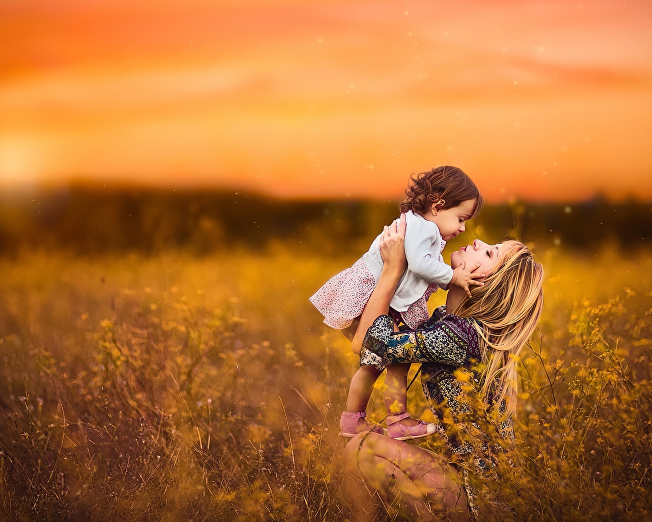 Девушка держит маленькую девочку на руках в поле на закате