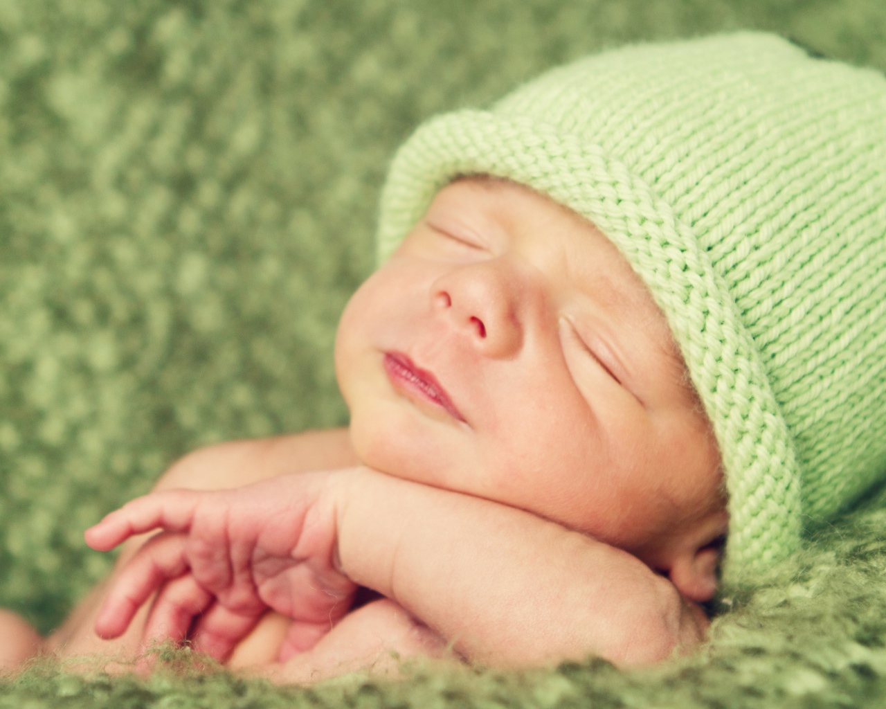 Зеленая вязаная шапка на голове у спящего ребенка 