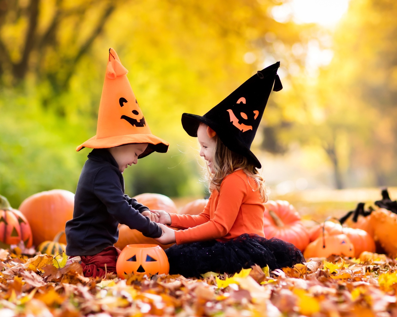 Маленькие мальчик и девочка в костюмах на Хэллоуин сидят на листве