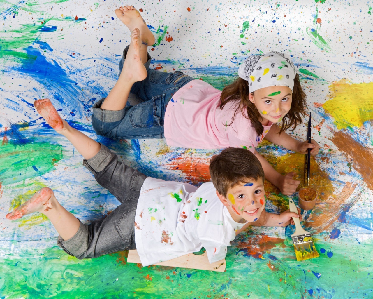 Маленькие мальчик и девочка рисуют красками на полу 