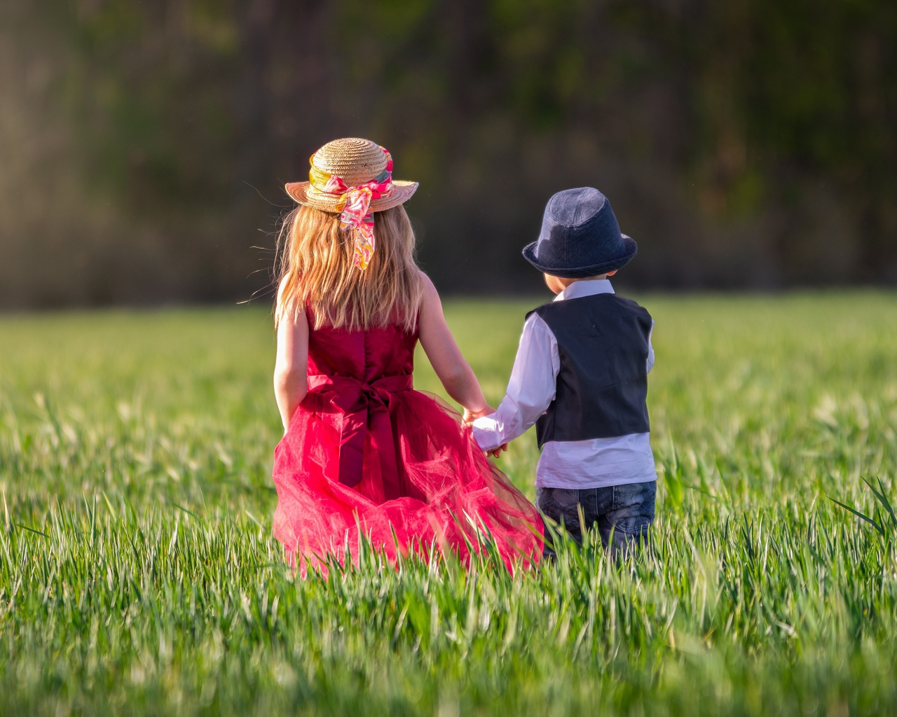 Маленькие мальчик и девочка идут по зеленому полю