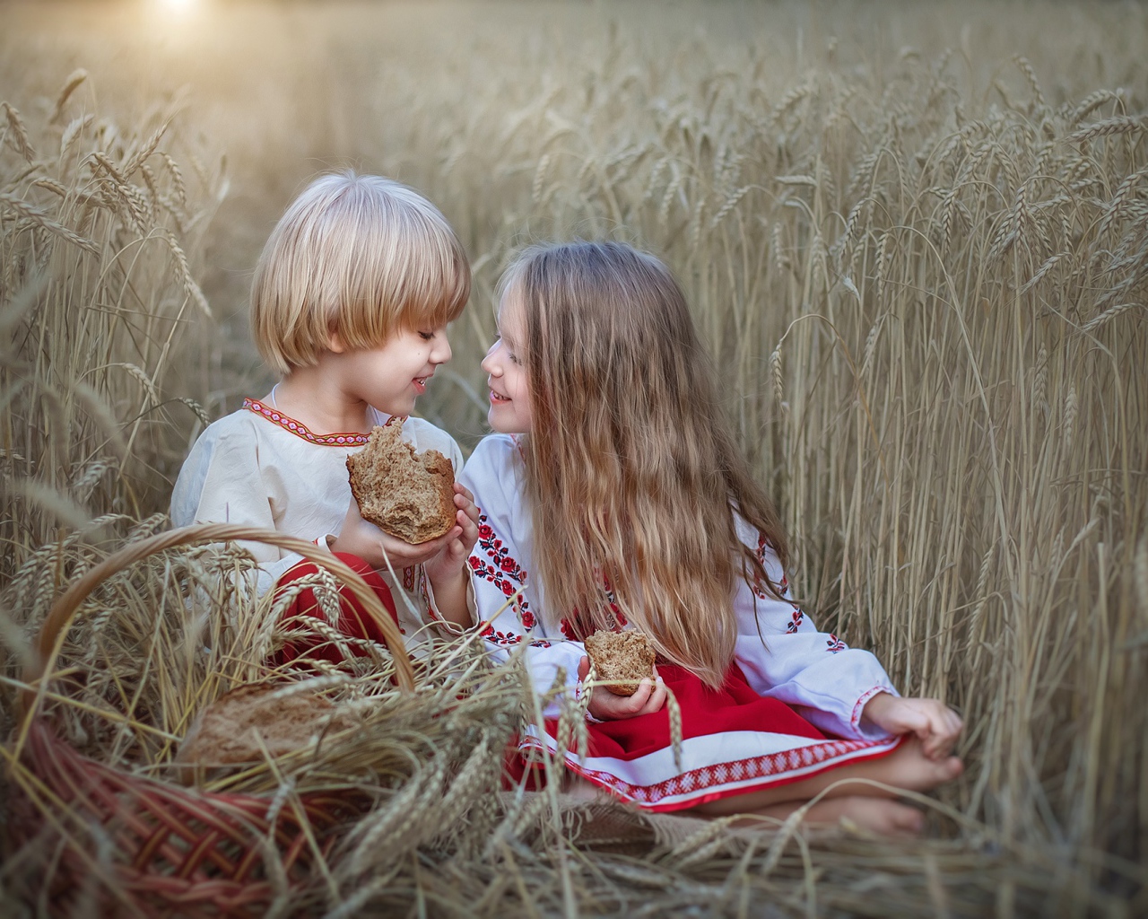 Маленькие мальчик и девочка с хлебом на пшеничном поле 