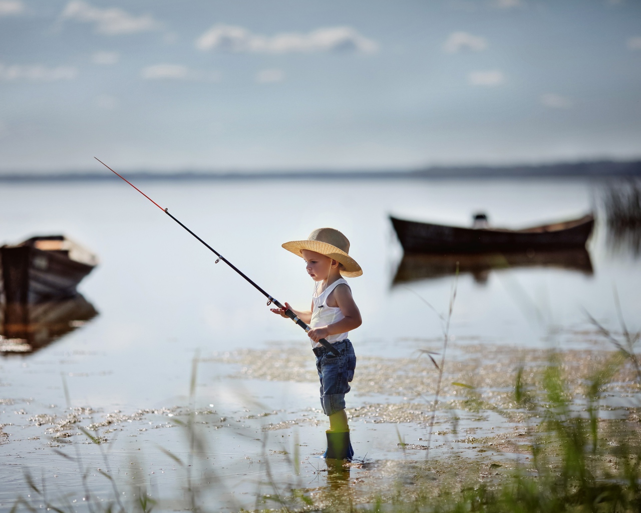 Маленький мальчик в шляпе ловит рыбу в озере 