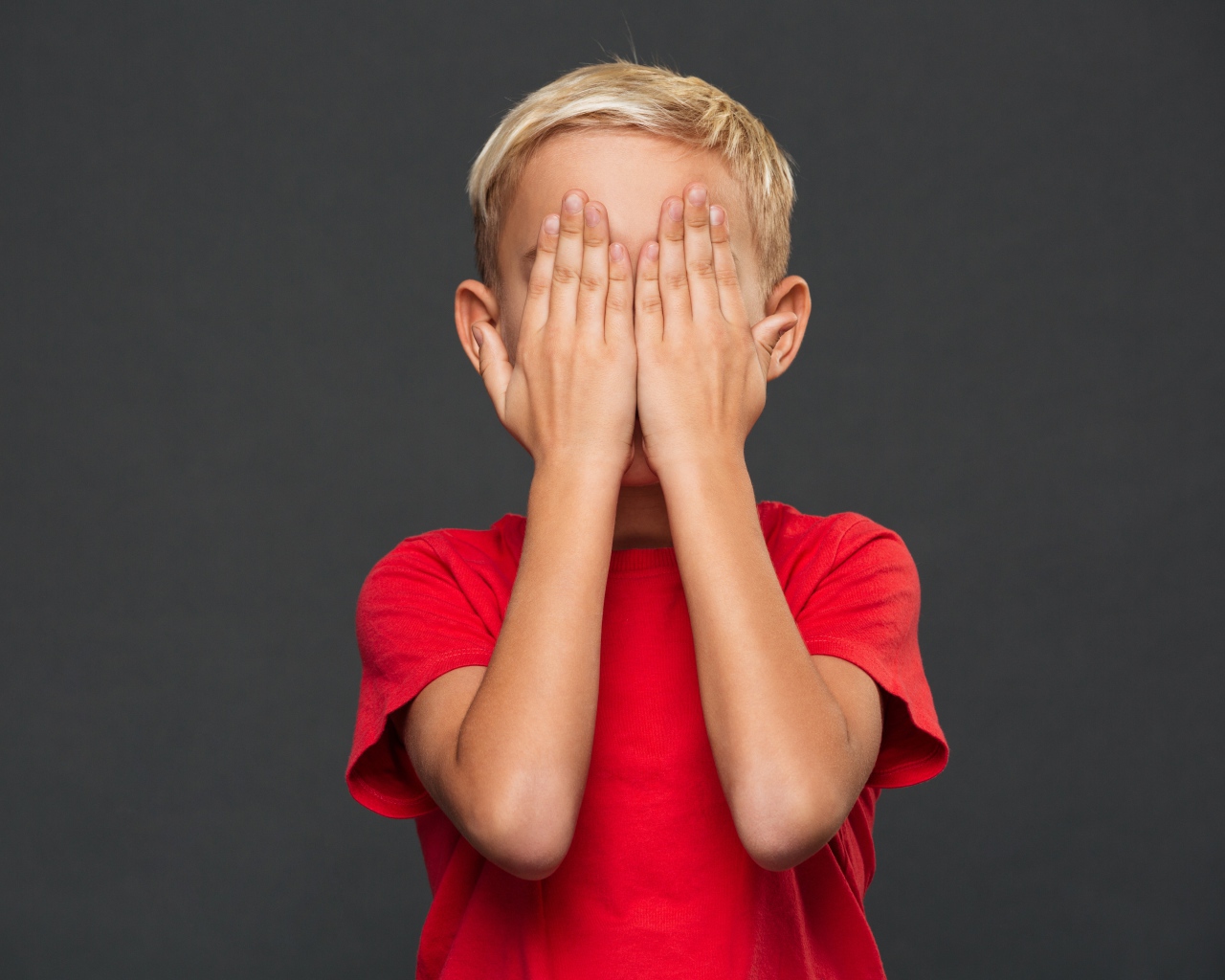 Маленький мальчик в красной футболке закрыл лицо руками 