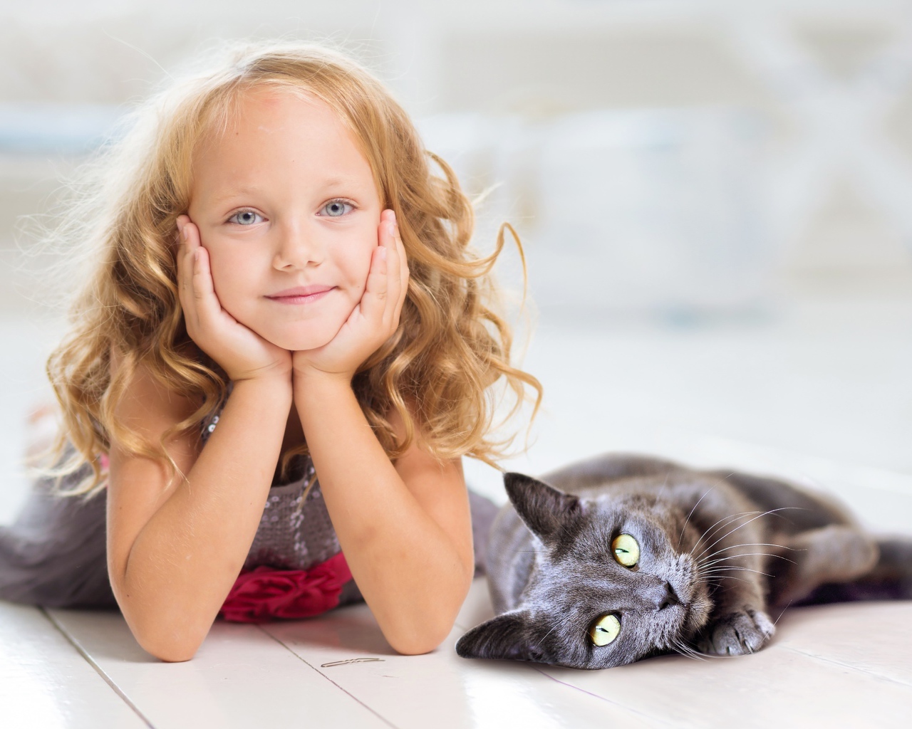 Маленькая милая голубоглазая девочка лежит на полу с котом
