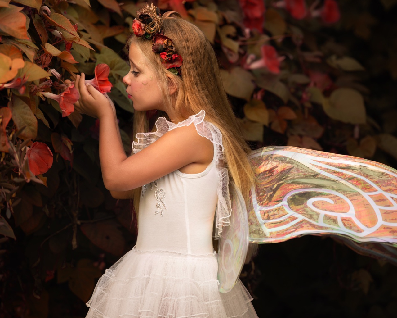 Маленькая девочка в костюме феи стоит у цветов