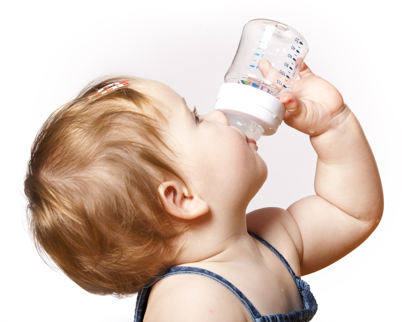 Маленькая девочка пьет молоко с бутылочки на белом фоне