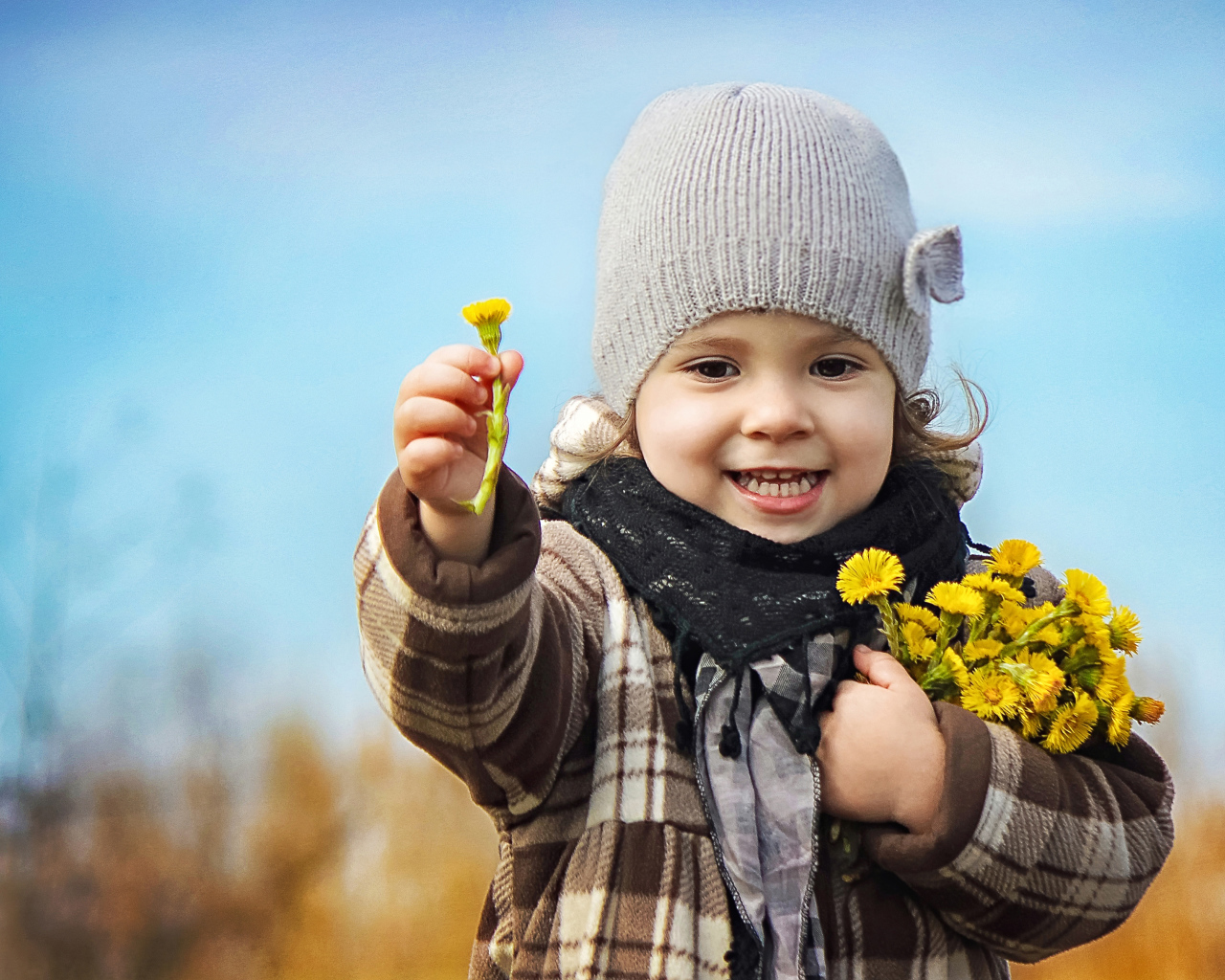 Маленькая девочка в шапке с желтыми цветами в руке