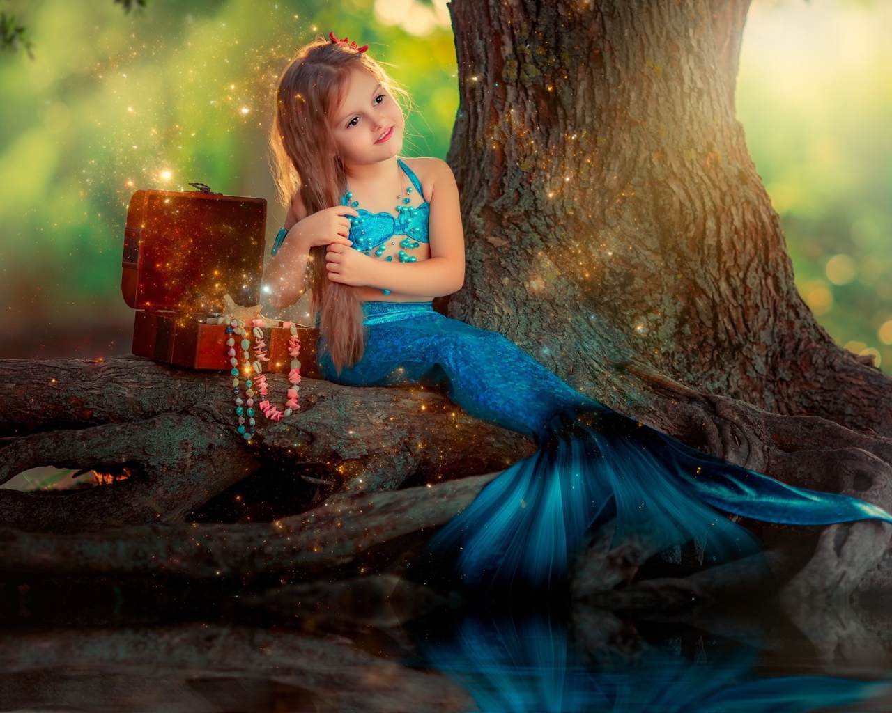 Маленькая девочка в костюме русалочки сидит у воды 