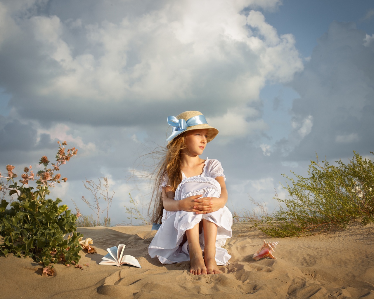 Маленькая девочка в белом платье сидит на песке 