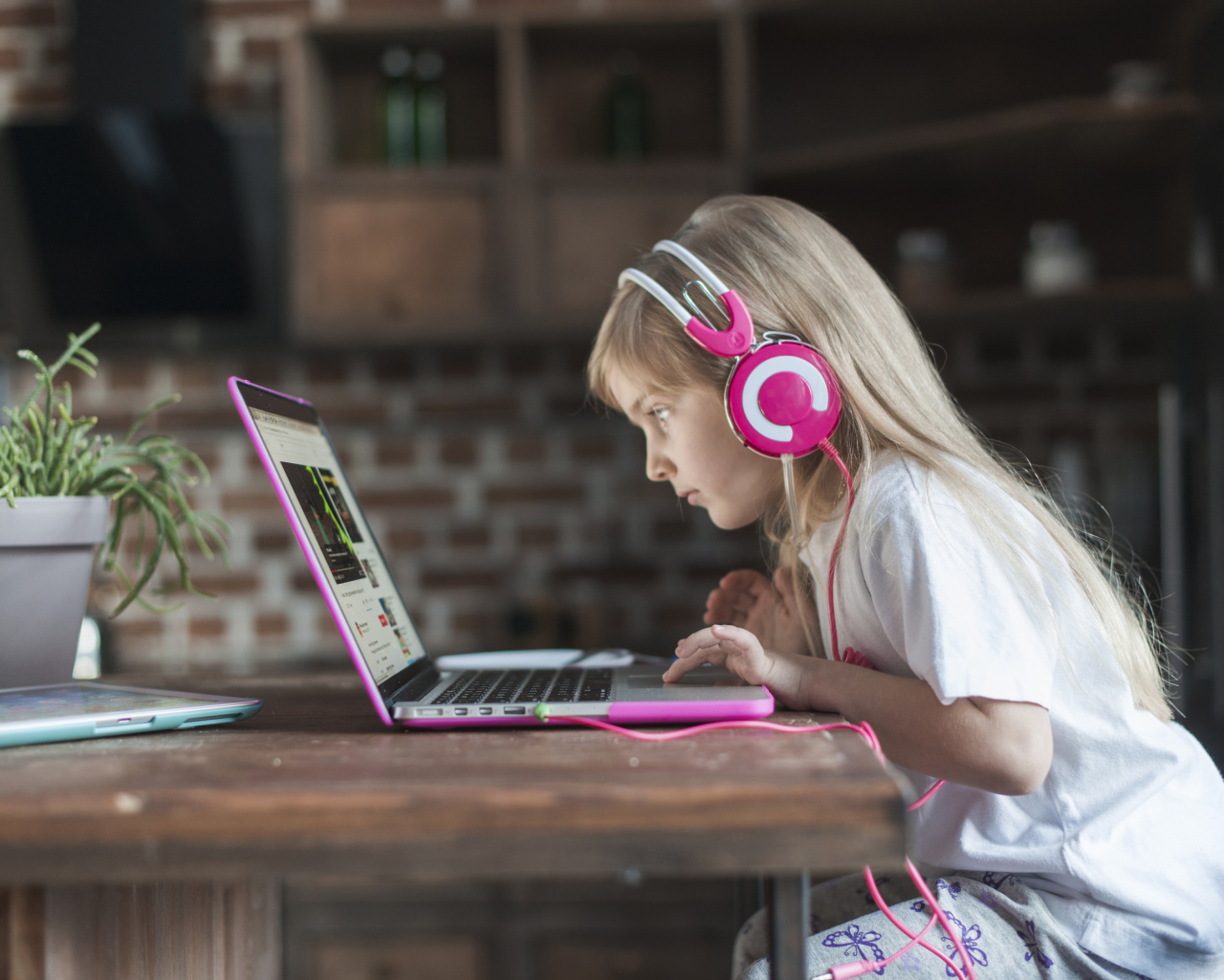 Маленькая девочка в наушниках сидит за ноутбуком