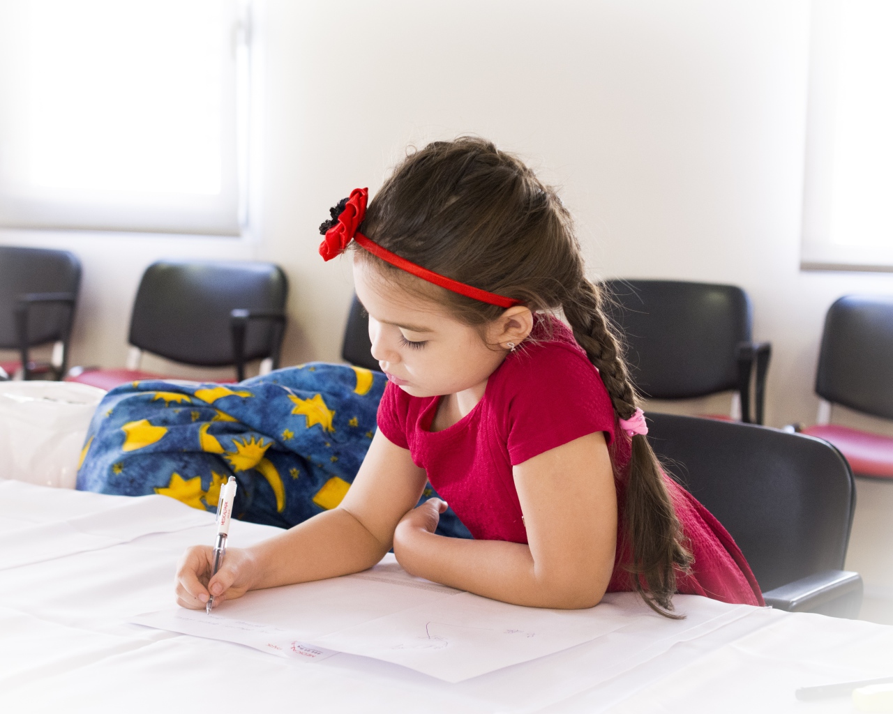 Маленькая девочка в красном платье рисует за столом