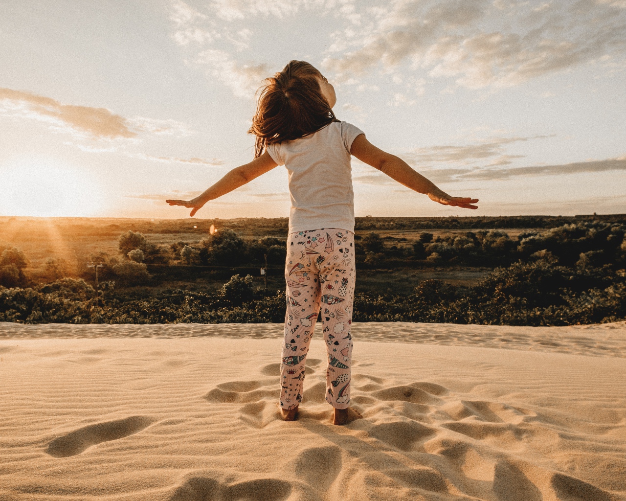Маленькая девочка стоит на песку в лучах солнца