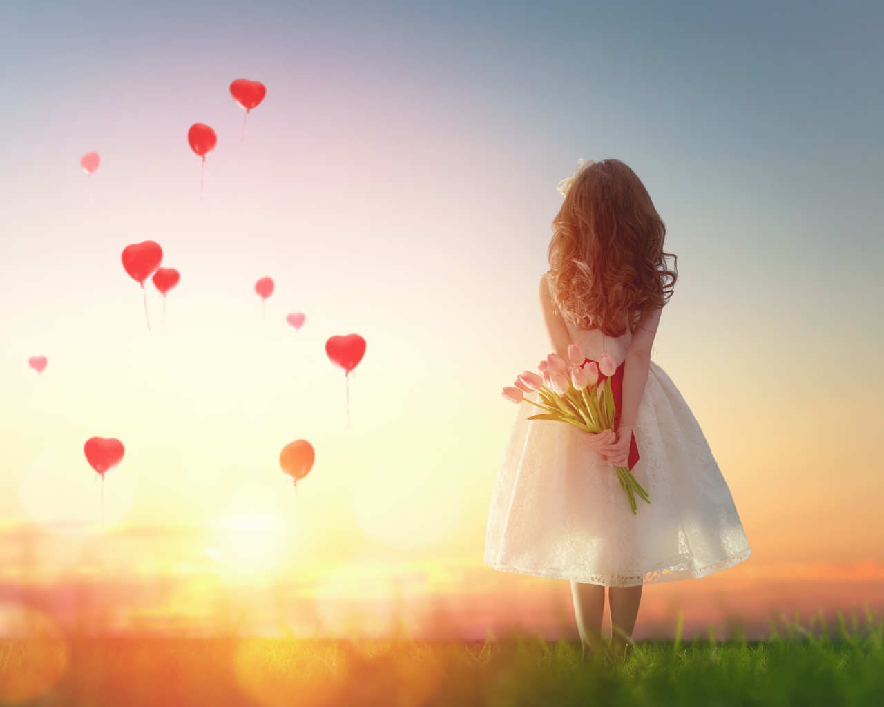 Маленькая девочка с букетом тюльпанов на фоне неба с воздушными шарами