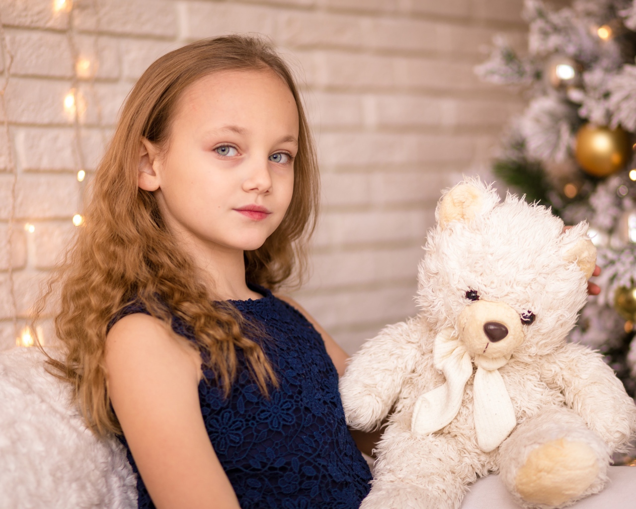 Маленькая девочка с мишкой сидит у наряженной ели 