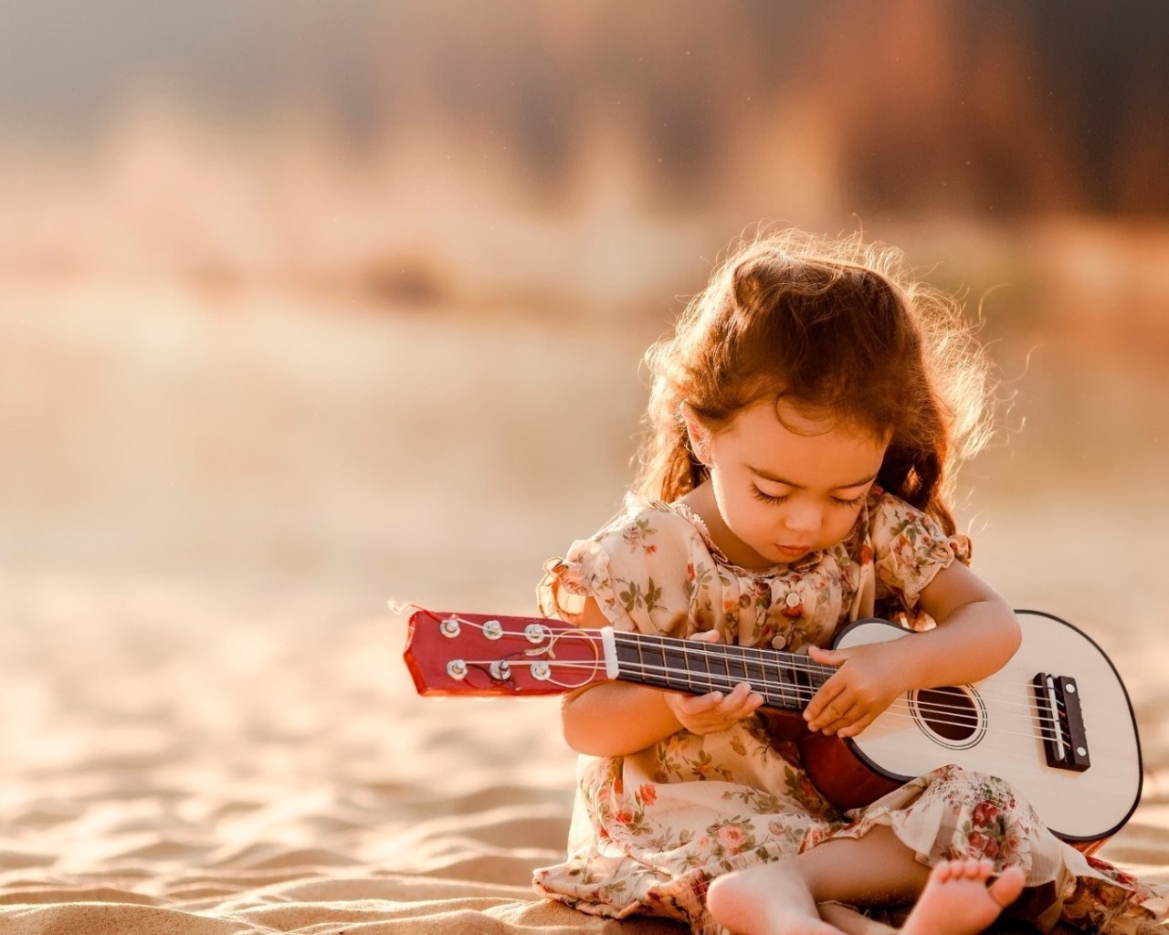 Маленькая девочка с гитарой сидит на песке 
